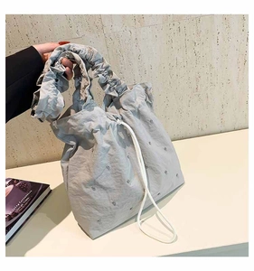 Detail of light gray tote bag with rivet studs, pleat handles and drawstring closure