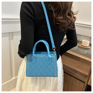 Detail of sky blue quilted handbag with gold heart embroidery worn as crossbody bag