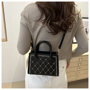 Detail of black quilted handbag with heart embroidery and golden hardware accents