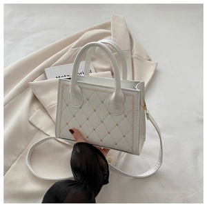 Detailed view of white leather quilted handbag with gold heart embroidery and strap
