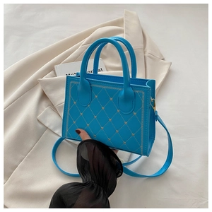 Detail of bright blue quilted handbag featuring gold heart accents and dual cylindrical handles
