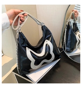 Detail of glossy black shoulder bag featuring a white leather butterfly and silver studs