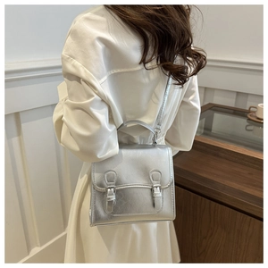 Detail einer silbernen Metallic-Tasche mit Schnalle und Tragegriff beim Tragen