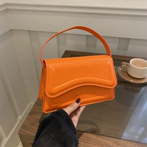 Modern orange glossy handbag with wavy embossed patterns and stylish accordion side folds