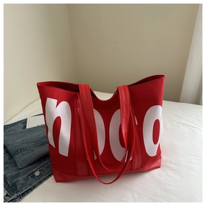 Détail du grand sac cabas rouge avec lettrage NOC blanc sur une surface blanche nette