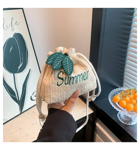 Detail of straw bucket bag with green leaf charms and Summer embroidery