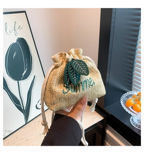 Detailed close-up of straw bucket bag featuring green leaf decor and Summer embroidery