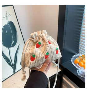 Close-up of strawberry embroidery detail on ivory woven straw bucket bag with drawstring