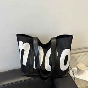 Grand sac cabas en nylon noir avec lettres blanches sur un canapé en cuir moderne