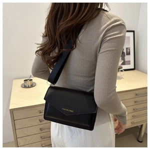 Close-up of black PU leather flap bag with gold FASHION & BAGS logo and wide strap
