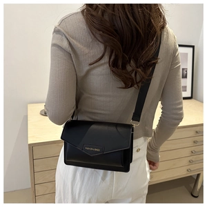 Close-up of black crossbody bag with gold text on a wide strap and minimalist design