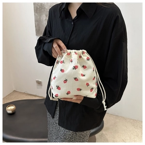 Detail of strawberry print corduroy drawstring bucket bag held by a model in a cozy setting