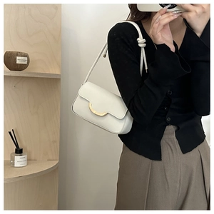 Close-up of a white leather shoulder bag with gold hardware and unique shoulder strap knots