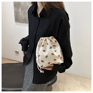 Detailed view of white corduroy mini bucket bag with red strawberry print on model