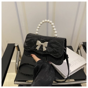 Detail of black pleated crossbody bag with pearl handle and silver bow decoration