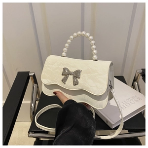 Detailed shot of cream PU leather crossbody bag with pearl handle and bow clasp detail
