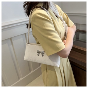 Detail of a creamy white pleated shoulder bag with a silver metallic bow decoration