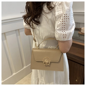 Chic beige crossbody bag with gold ring lock shown on model in white lace dress