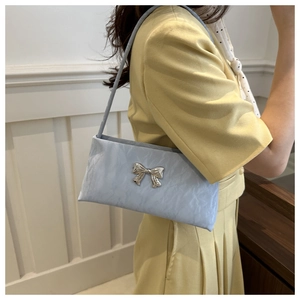 Detail of light blue pleated shoulder bag with silver bow buckle worn by model