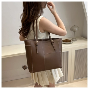 Detail of deep brown tote bag with white stitching and gold buckle on shoulder strap