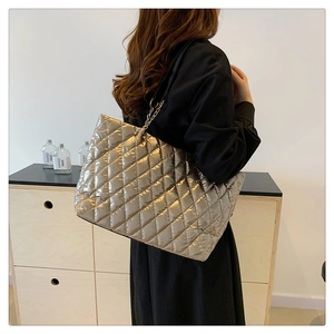Detail of silver metallic puffer tote bag with quilted pattern and chain strap on shoulder