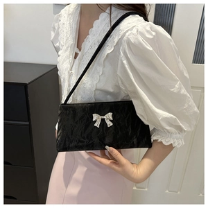 Detail of black pleated shoulder bag featuring a 3D silver metal bow and shiny finish