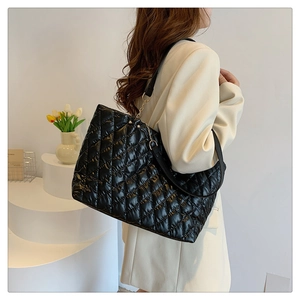 Detail view of black quilted tote bag with golden chain strap on a minimalist stage