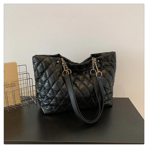 Detail of black quilted tote bag featuring glossy nylon fabric and metal chain strap