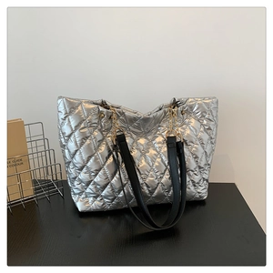 Detail of silver quilted tote bag with black straps and chain decoration on desk