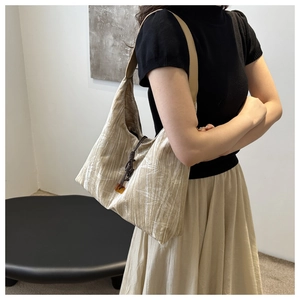 Detail of beige pleated fabric shoulder bag with dark brown drawstring and soft texture