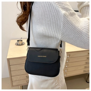 Close-up of black crossbody saddle bag showing fine stitching and gold lettering detail