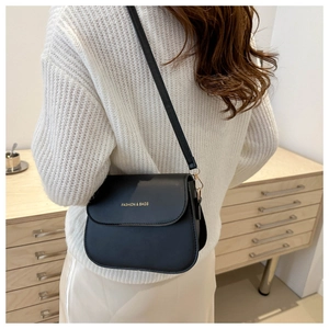 Model wearing a black leather saddle crossbody bag with gold fashion text and hardware