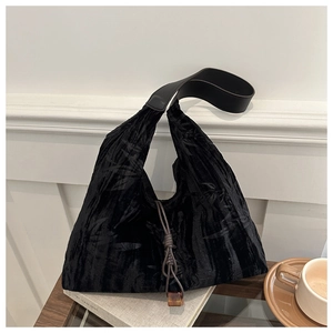 Detail of black tote bag featuring textured leaf patterns and brown knot pendant