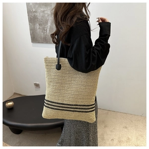 Detail of a large straw tote bag with black stripes and long shoulder straps shown on a model