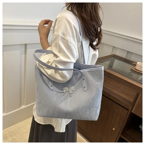 Detail of light blue pleated tote bag with silver butterfly charm on a female model