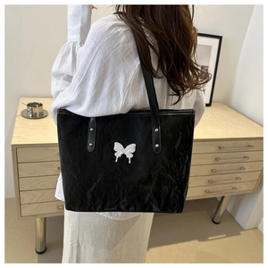 Detail of black pleated tote bag featuring a metallic butterfly logo and slim straps