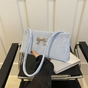 Light blue pleated fabric shoulder bag with silver bow accessory in a modern setting