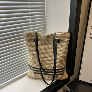 Chic beige woven straw tote bag with black stripes and leather straps on white window ledge