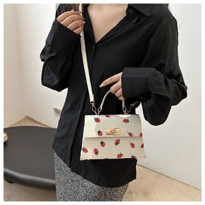 Detail of strawberry print corduroy crossbody bag with golden twist lock on a model