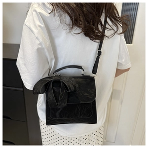 Detail view of the black bow backpack showing unique wrinkled leather texture on a model