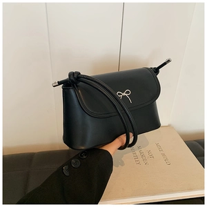 Close-up of black leather crossbody bag with silver bow ornament and knotted strap detail
