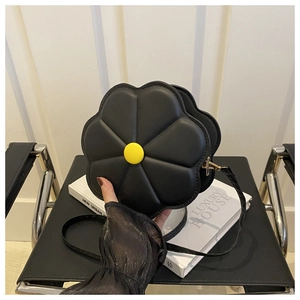 Détail d'un sac bandoulière noir en forme de fleur avec un bouton jaune sur un livre