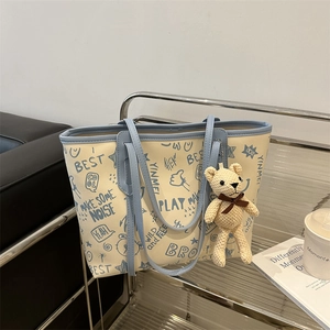 Minimalist cream tote bag with blue graffiti print and cute bear charm for daily commute