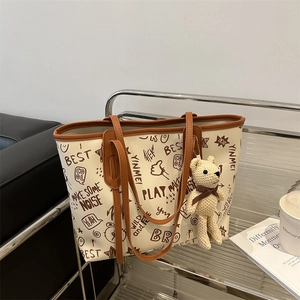 Minimalist large tote bag with graffiti print and bear charm on metal shelf