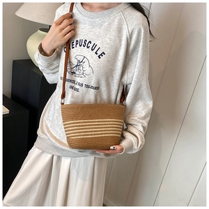 Detail of a brown woven bucket bag with beige stripes and slim shoulder strap