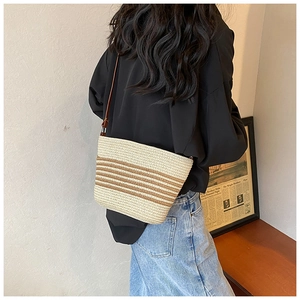 Detail view of woven straw bucket bag with brown stripes and leather strap on model