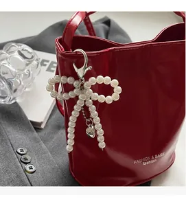 Detail of beaded bow pendant with silver lobster clasp on a red glossy leather handbag