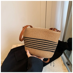 Detail view of woven straw bucket bag with black stripes and adjustable leather strap
