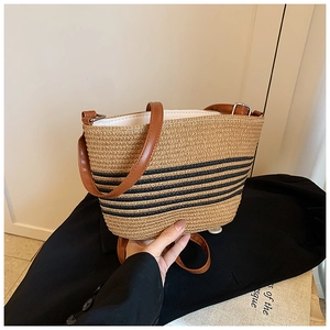 Detail of hand-woven straw tote with black stripes and adjustable brown leather strap
