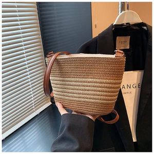 Detail shot of striped straw bucket bag with brown leather strap and metal buckles